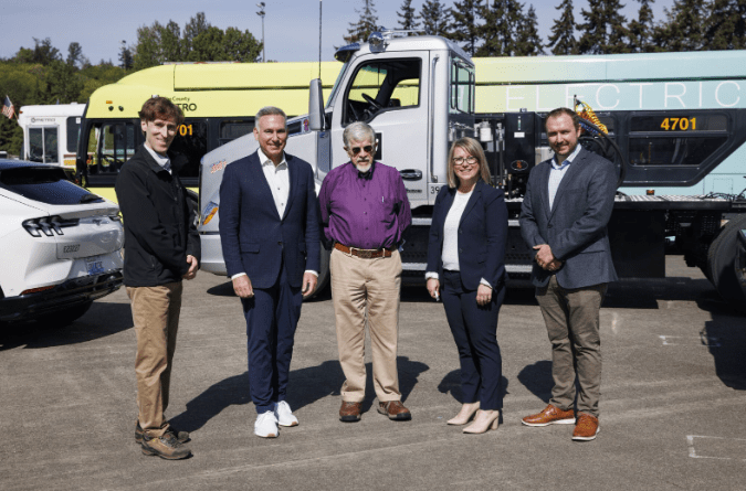 Group of county leaders stands in a row in front of a bus with a wrapper that says Electric.